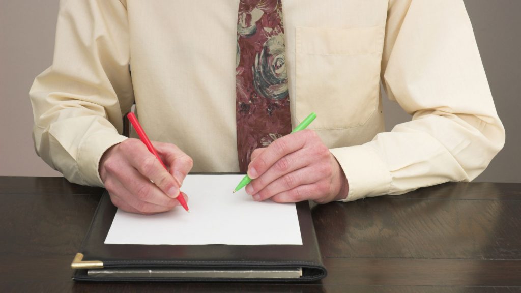 Man holding a pen in both hands over a piece of paper